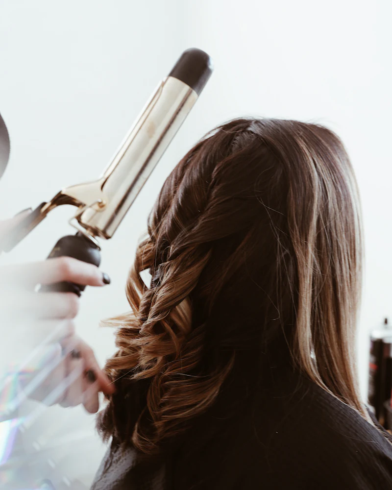 Stylist curling brown hair that has lighter pieces around the face