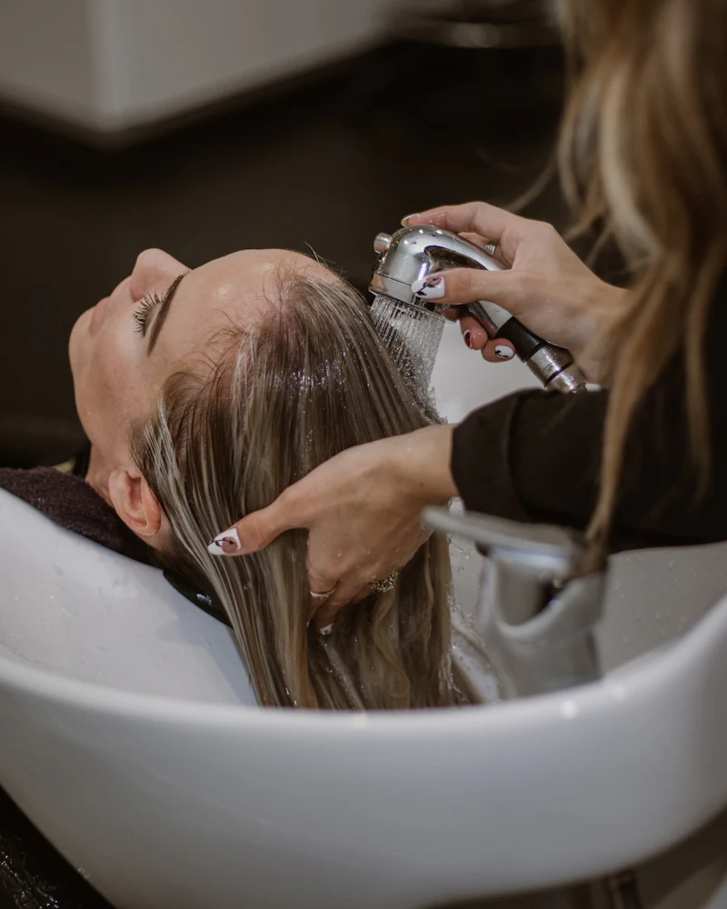 Woman reclined at a shampoo bowl while her wet blonde hair is rinsed